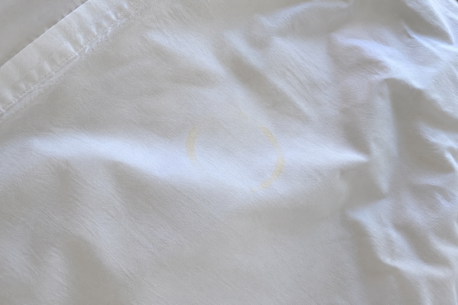 Auréole jaune de crème solaire incrustée sur un drap blanc en coton après lavage ménager